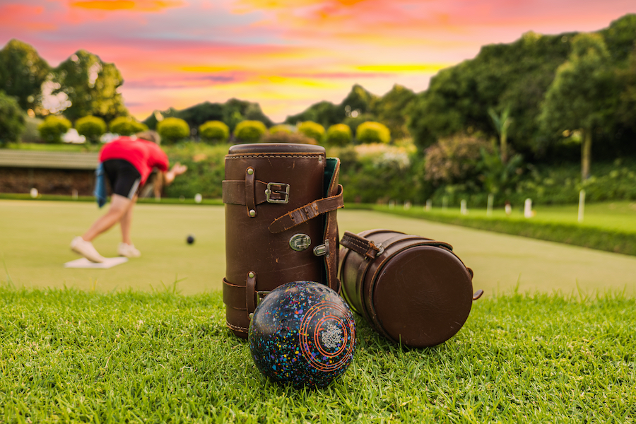 Lawn bowls leather bags and balls on the field side while players are playing at sunset